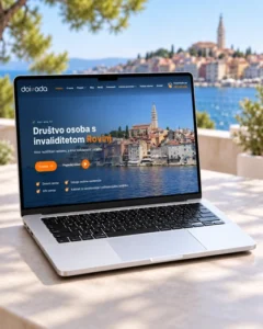 Web stranica Društva osoba s invaliditetom Rovinj prikazana na laptopu s panoramom Rovinja u pozadini.